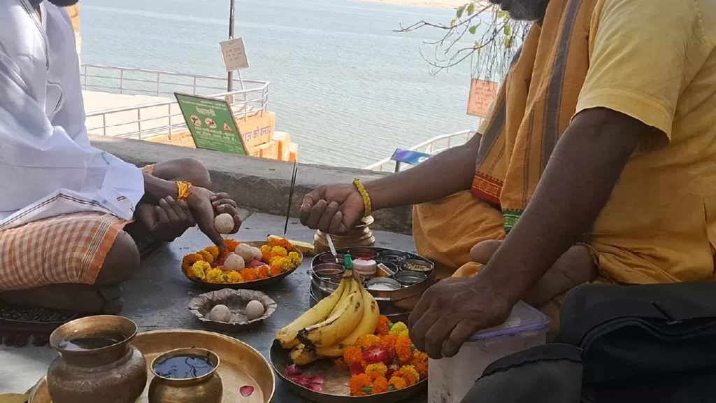 Image of A man prays with cupped hands during a riverside Shradh ritual (Tarpan), guided by a priest with offerings of Pind Daan- Pitrupaksha in Modern Life